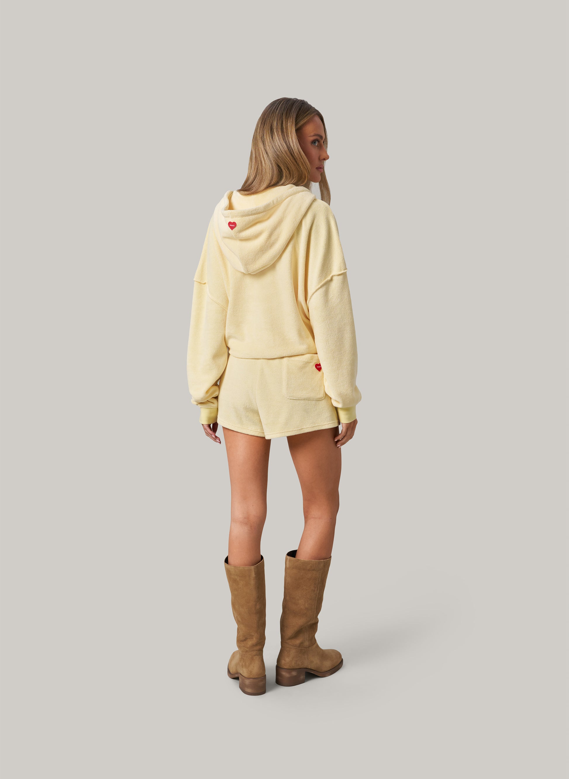 Person wearing a light yellow hoodie and brown boots on a plain background