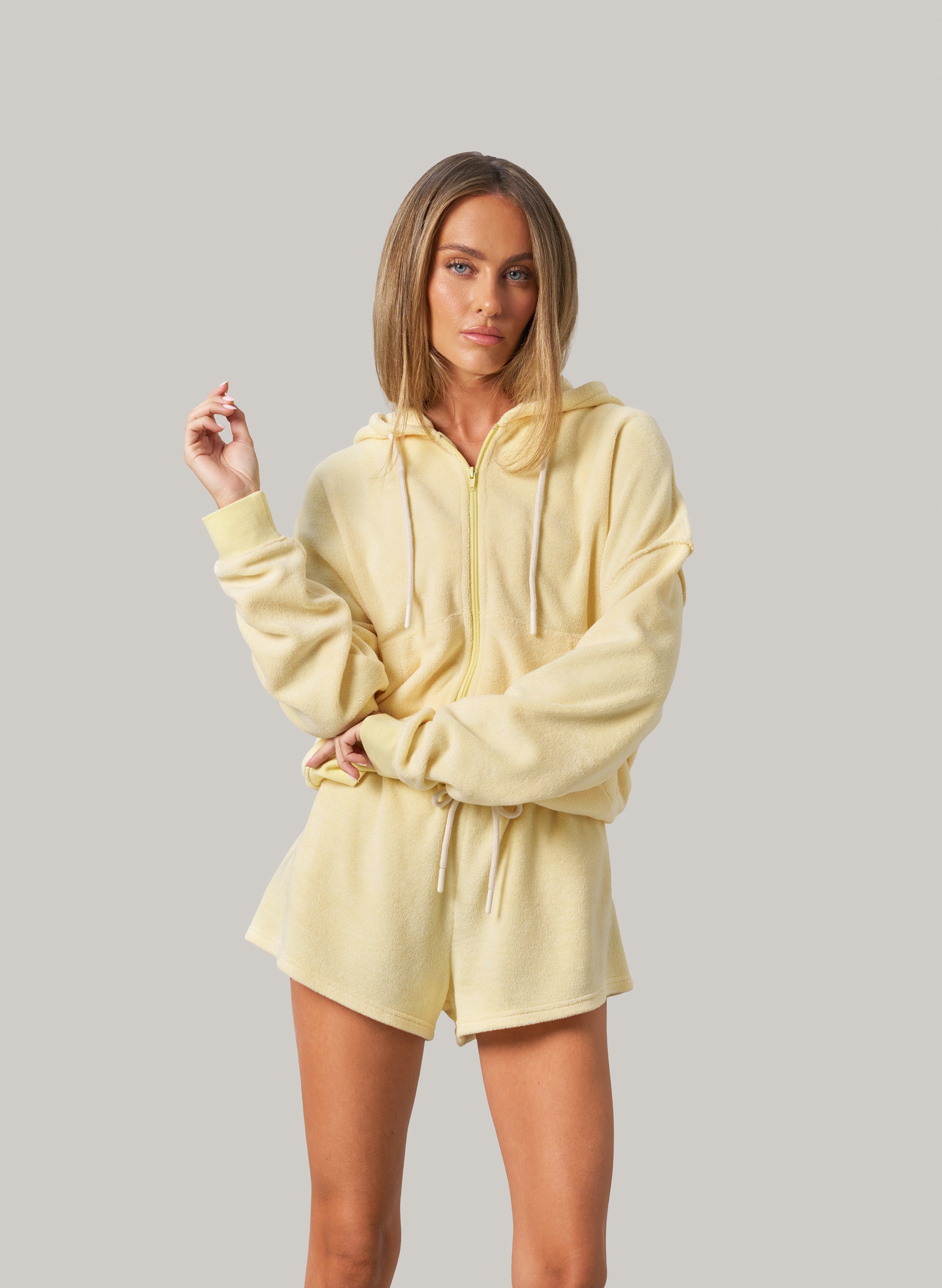 Woman wearing a light yellow hoodie and shorts set on a plain background