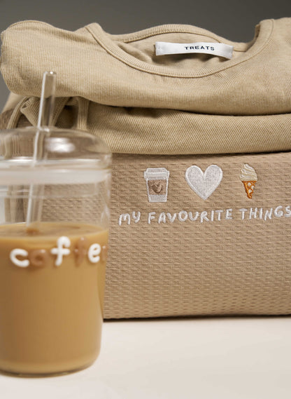 Beige embroidered bag with 'My Favourite Things' text and graphics, next to a glass of coffee.