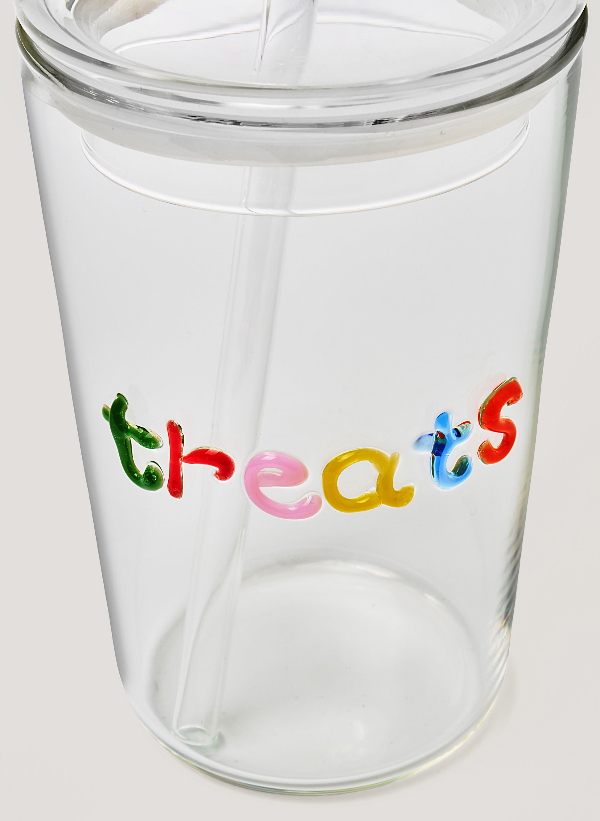Clear glass tumbler with colorful letters spelling 'threats' on a white background