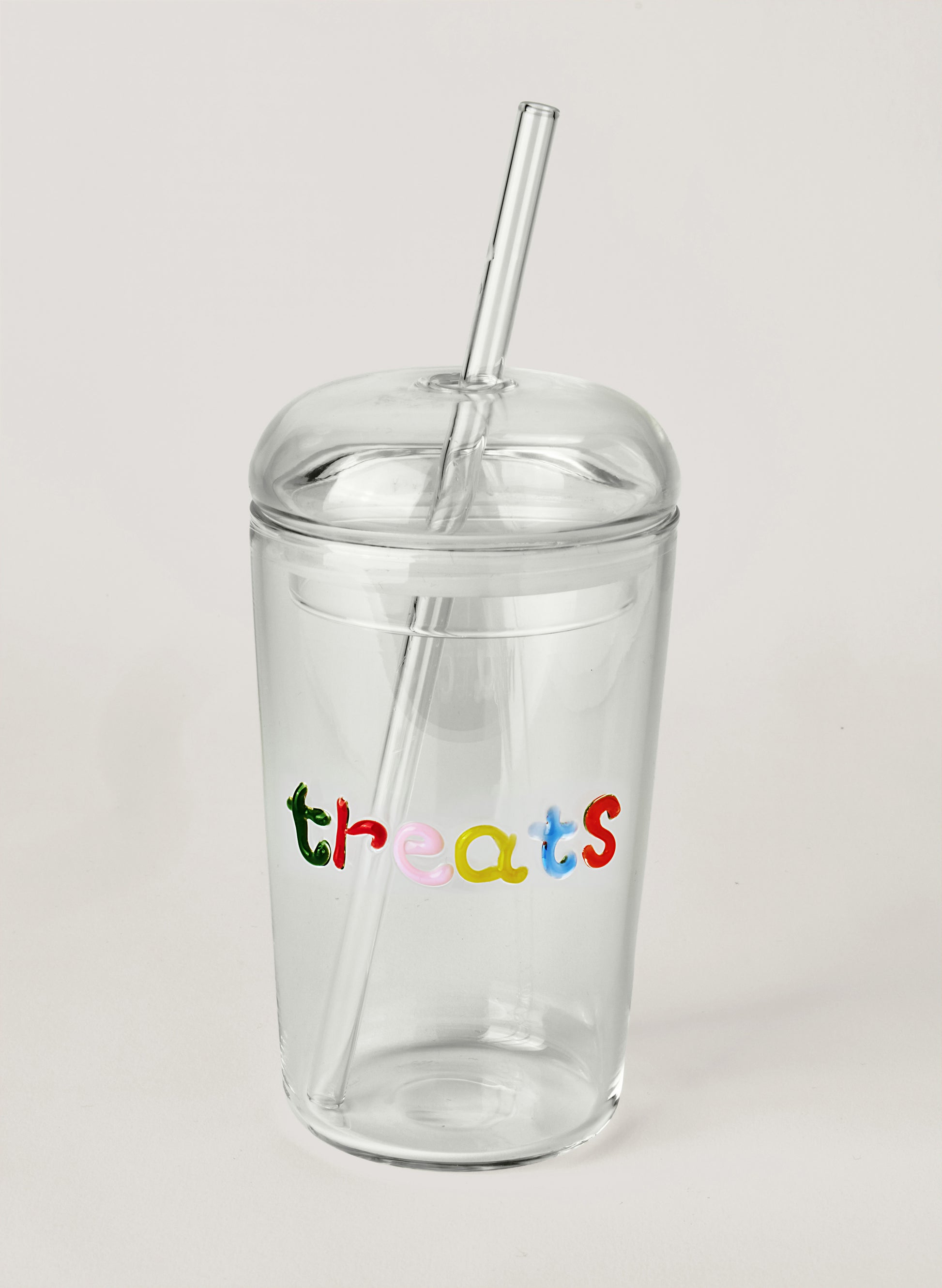 Clear glass tumbler with colourful text saying 'treats' with a straw, on a white background