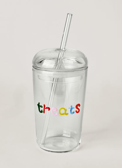 Clear glass tumbler with colourful text saying 'treats' with a straw, on a white background