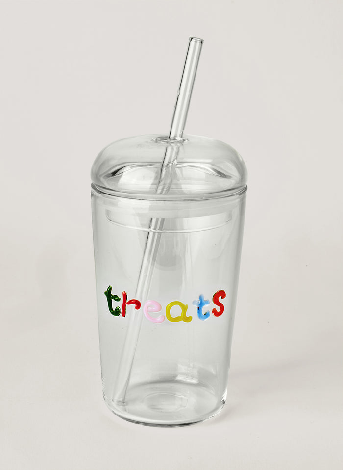 Clear glass tumbler with colourful text saying 'treats' with a straw, on a white background