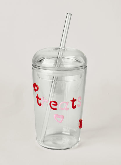 Clear glass tumbler with colourful text saying 'treats' and heart designs on a white background