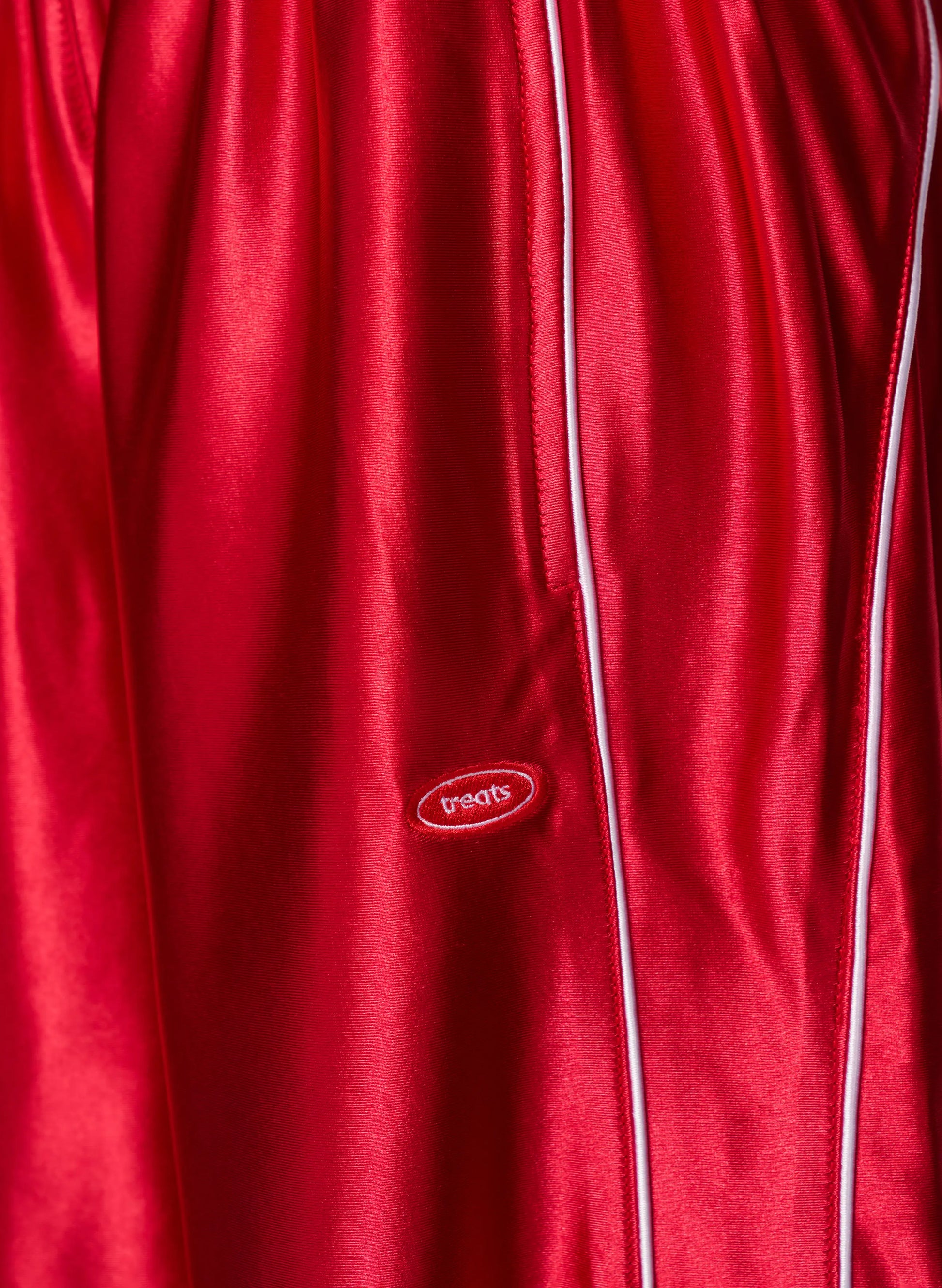 Close-up of a red satin or silk-like garment with white piping and a small oval 'paqos' logo patch near the center.