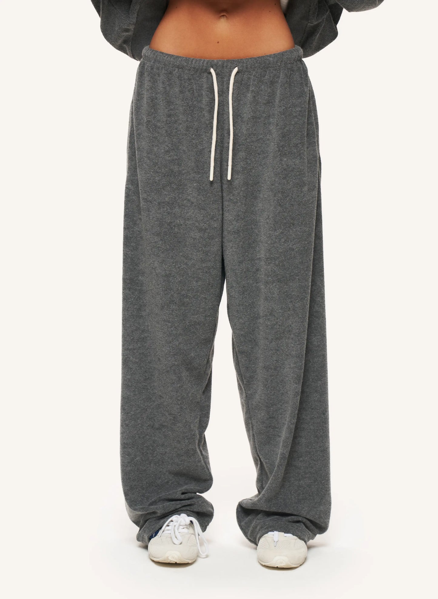 A person wearing loose dark gray sweatpants with a white drawstring, shown from the waist down against a plain light background.
