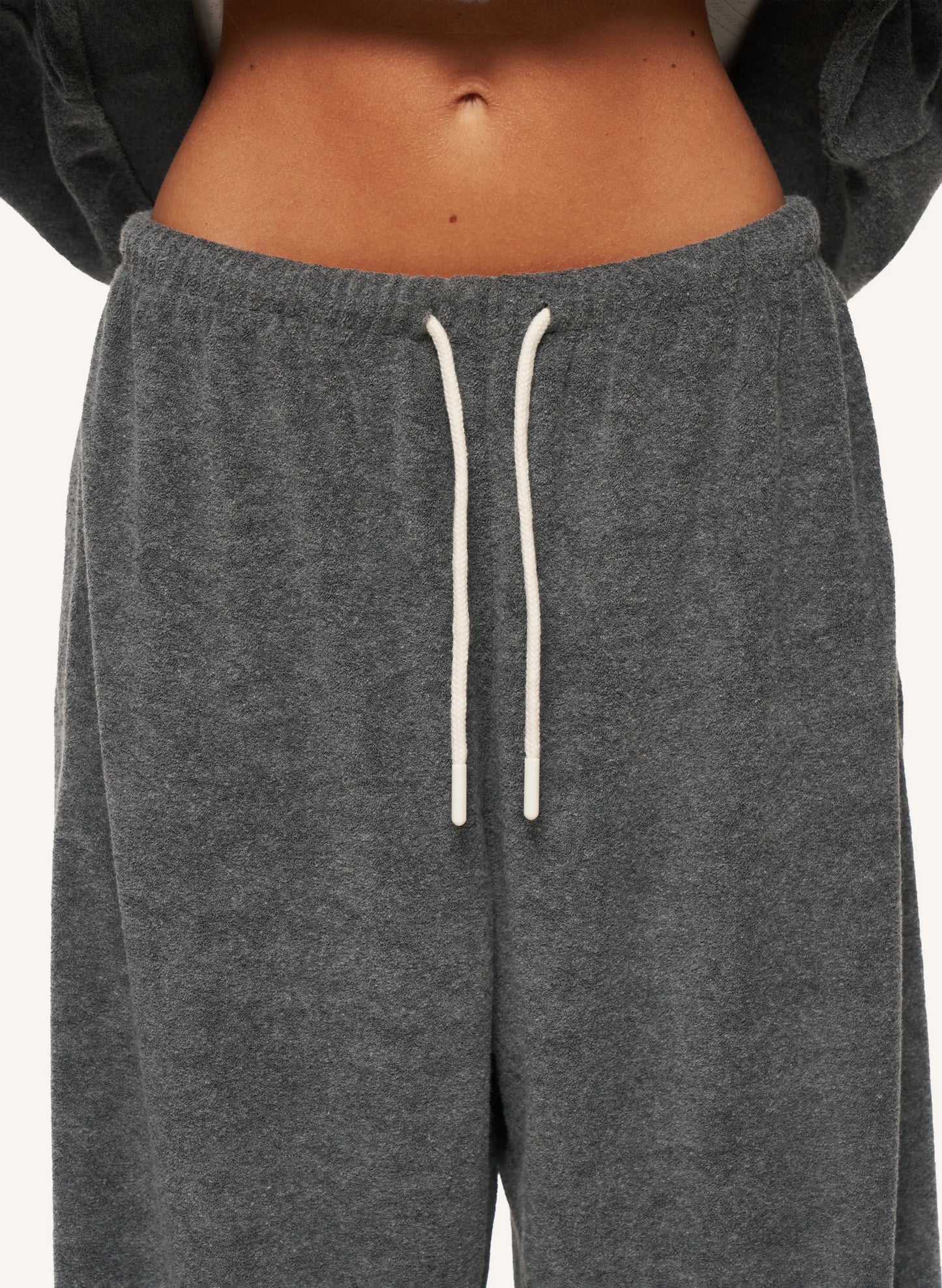 Close-up of a person wearing dark heather gray sweatpants with white drawstrings, cropped from the lower torso to upper thighs against a plain light background.
