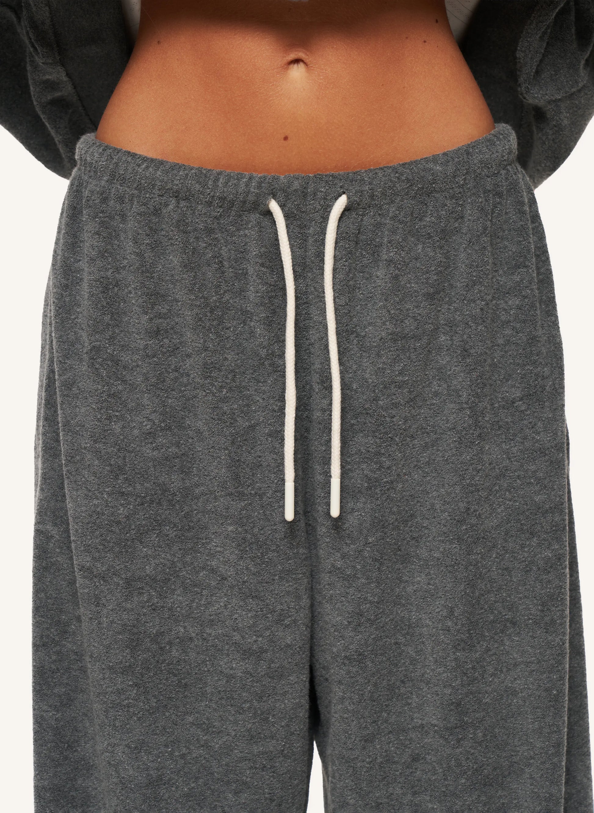 Close-up of a person wearing dark heather gray sweatpants with white drawstrings, cropped from the lower torso to upper thighs against a plain light background.