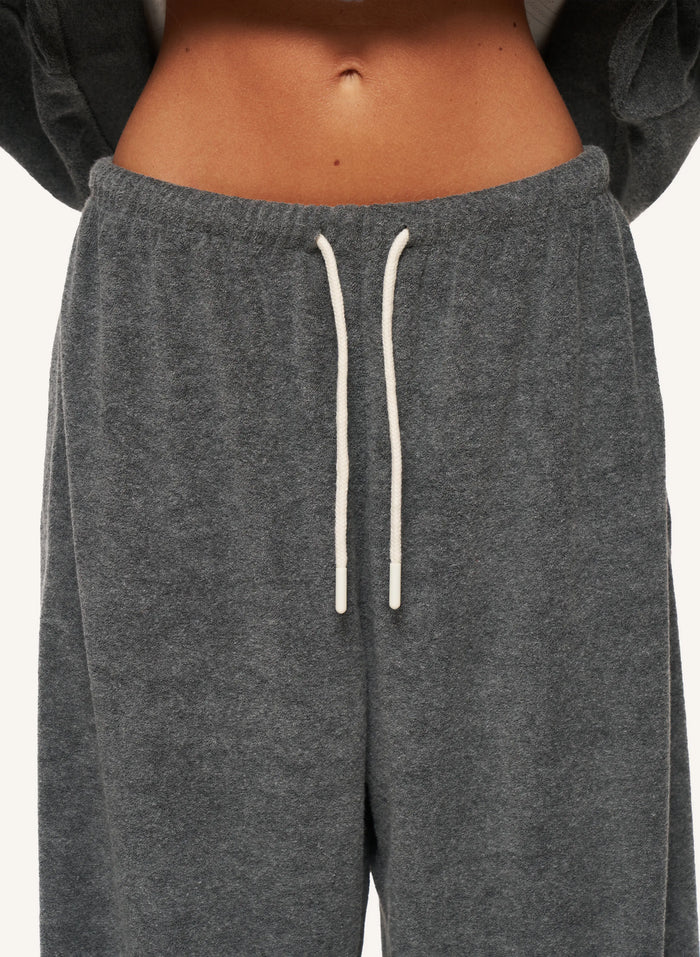 Close-up of a person wearing dark heather gray sweatpants with white drawstrings, cropped from the lower torso to upper thighs against a plain light background.