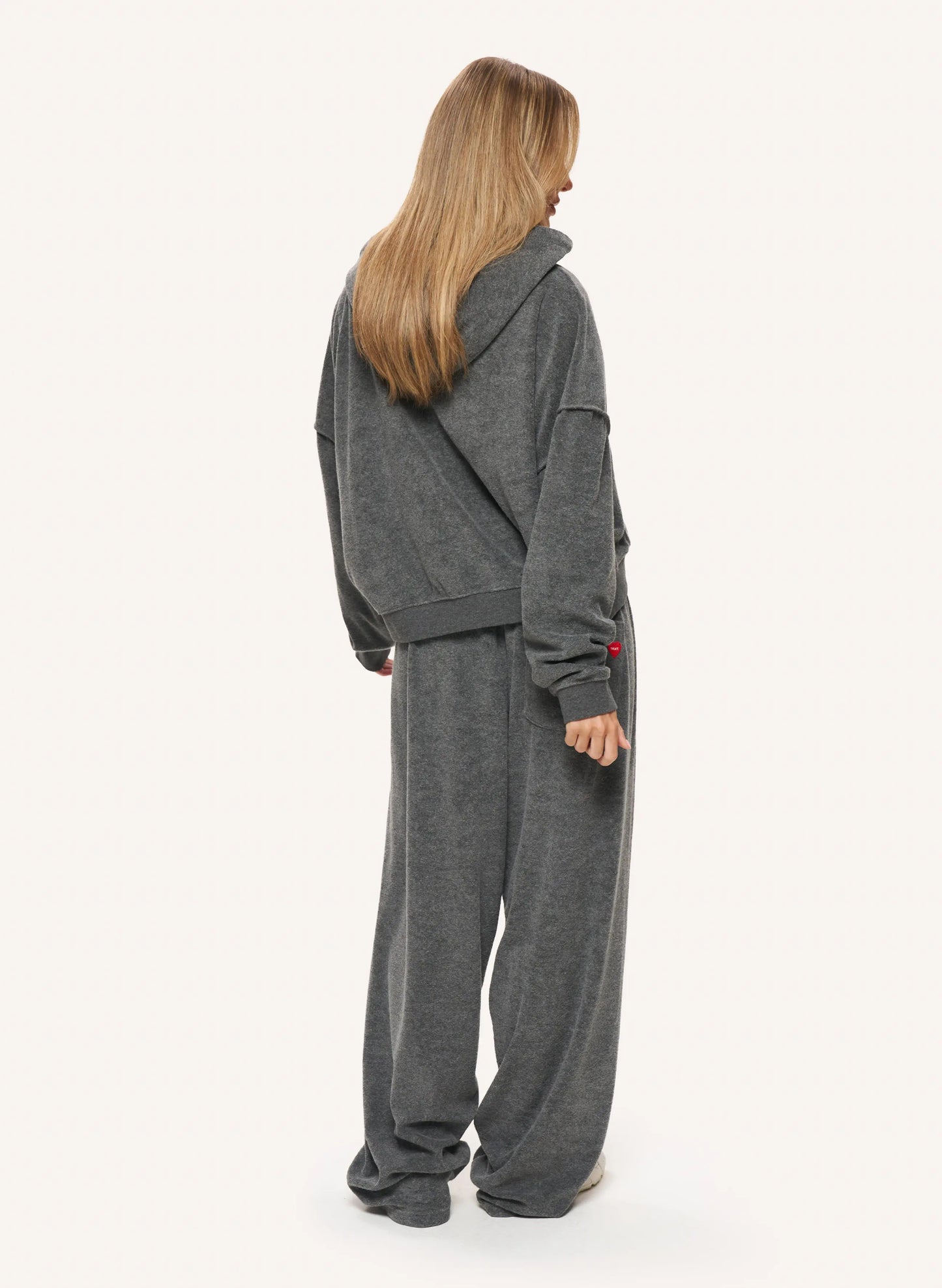 A woman shown from the back wearing a matching dark gray hooded sweatshirt and wide-leg sweatpants set, photographed against a plain light background.