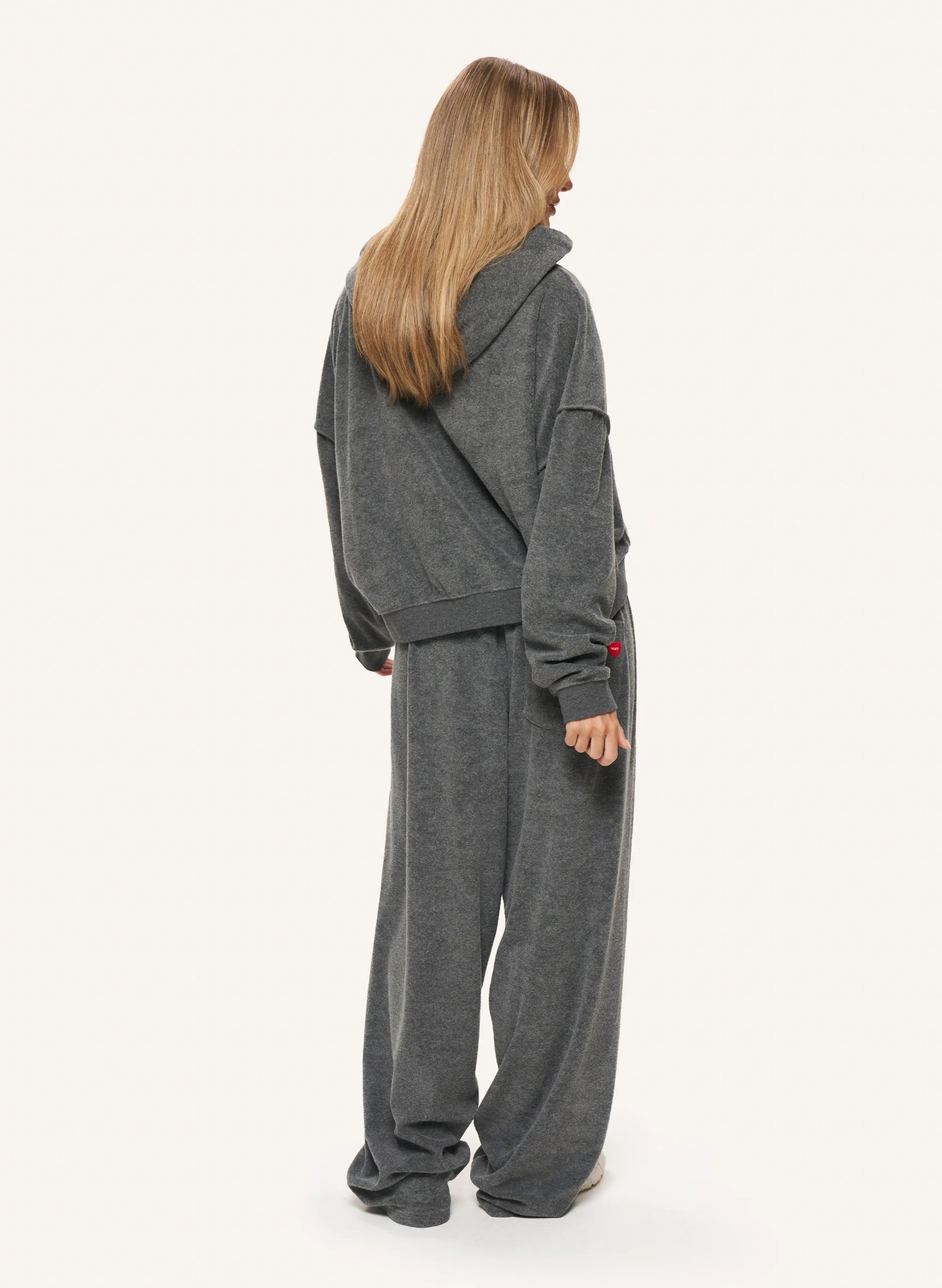 A woman shown from the back wearing a matching dark gray hooded sweatshirt and wide-leg sweatpants set, photographed against a plain light background.