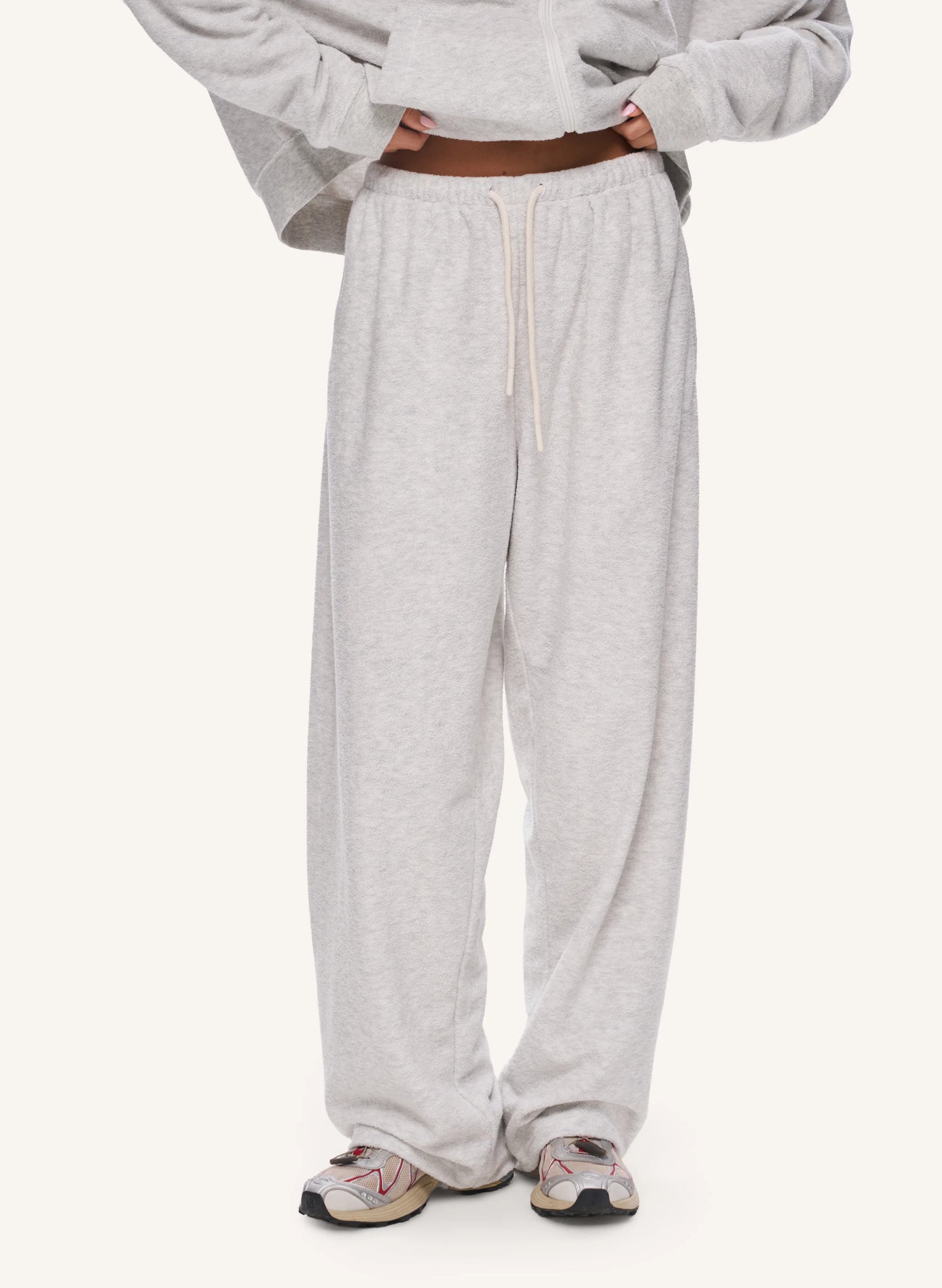 A person wearing light heather grey sweatpants with a drawstring waist, paired with a matching gray cropped hoodie and sneakers, shown from the chest down on a plain light background.