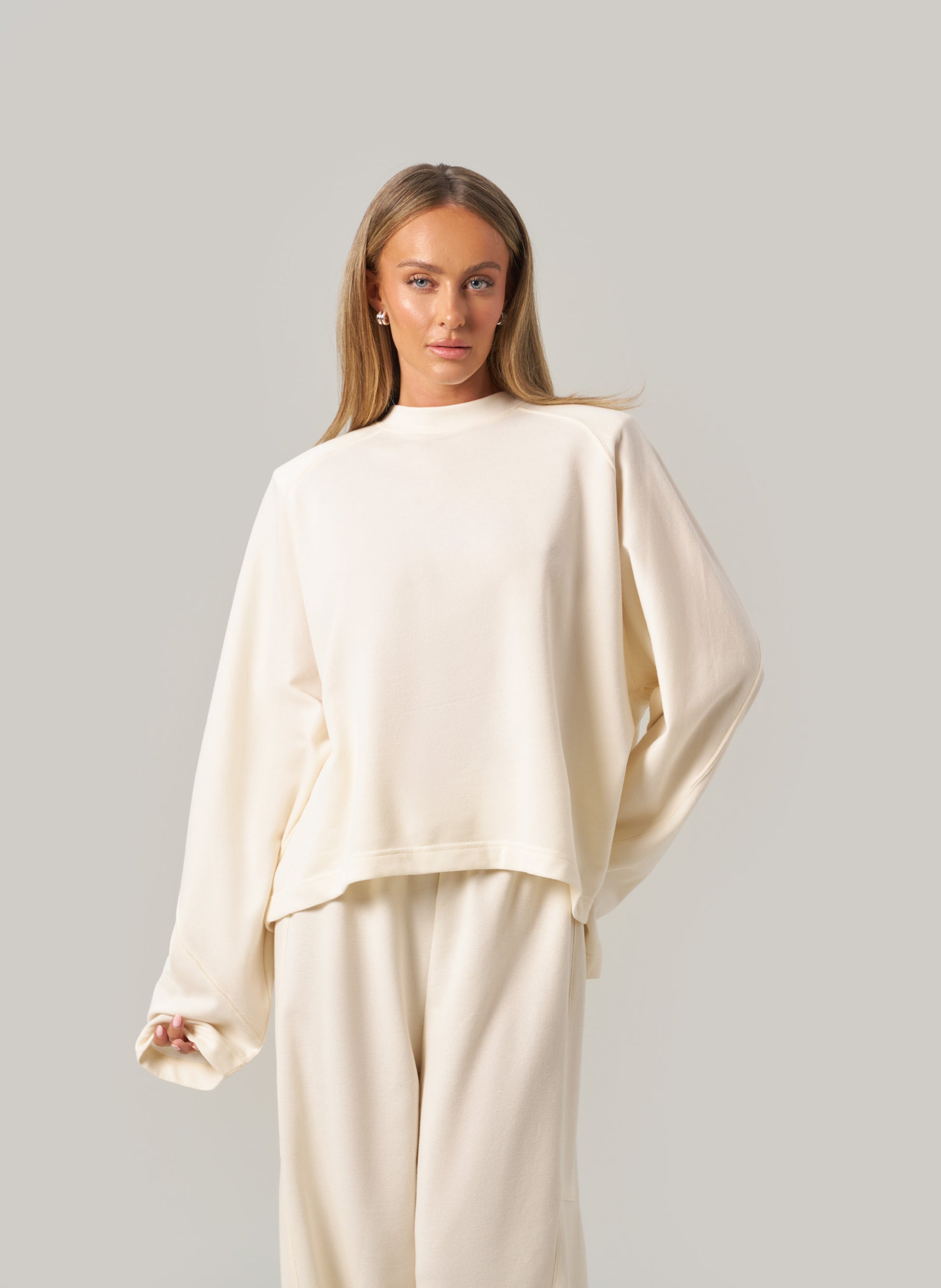 Woman wearing a cream-coloured outfit against a plain background