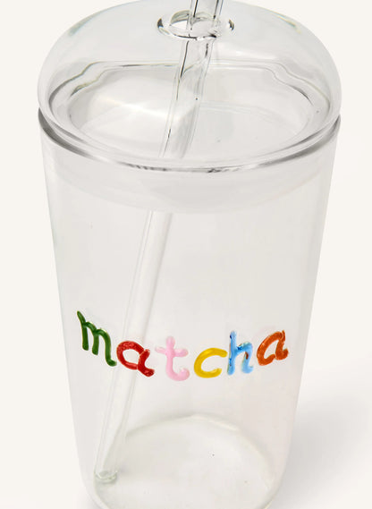 A clear glass tumbler with a matching clear lid and straw, featuring the word 'matcha' printed on the front in colorful lowercase letters.