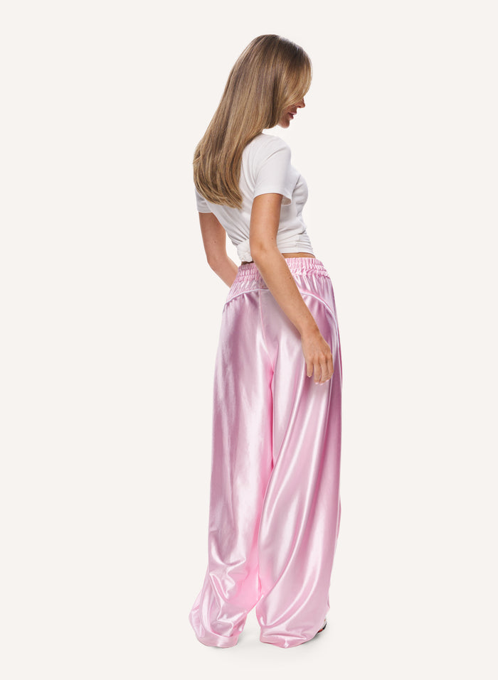 A woman shown from the back wearing shiny light pink wide-leg satin pants and a white cropped T-shirt against a plain light background.