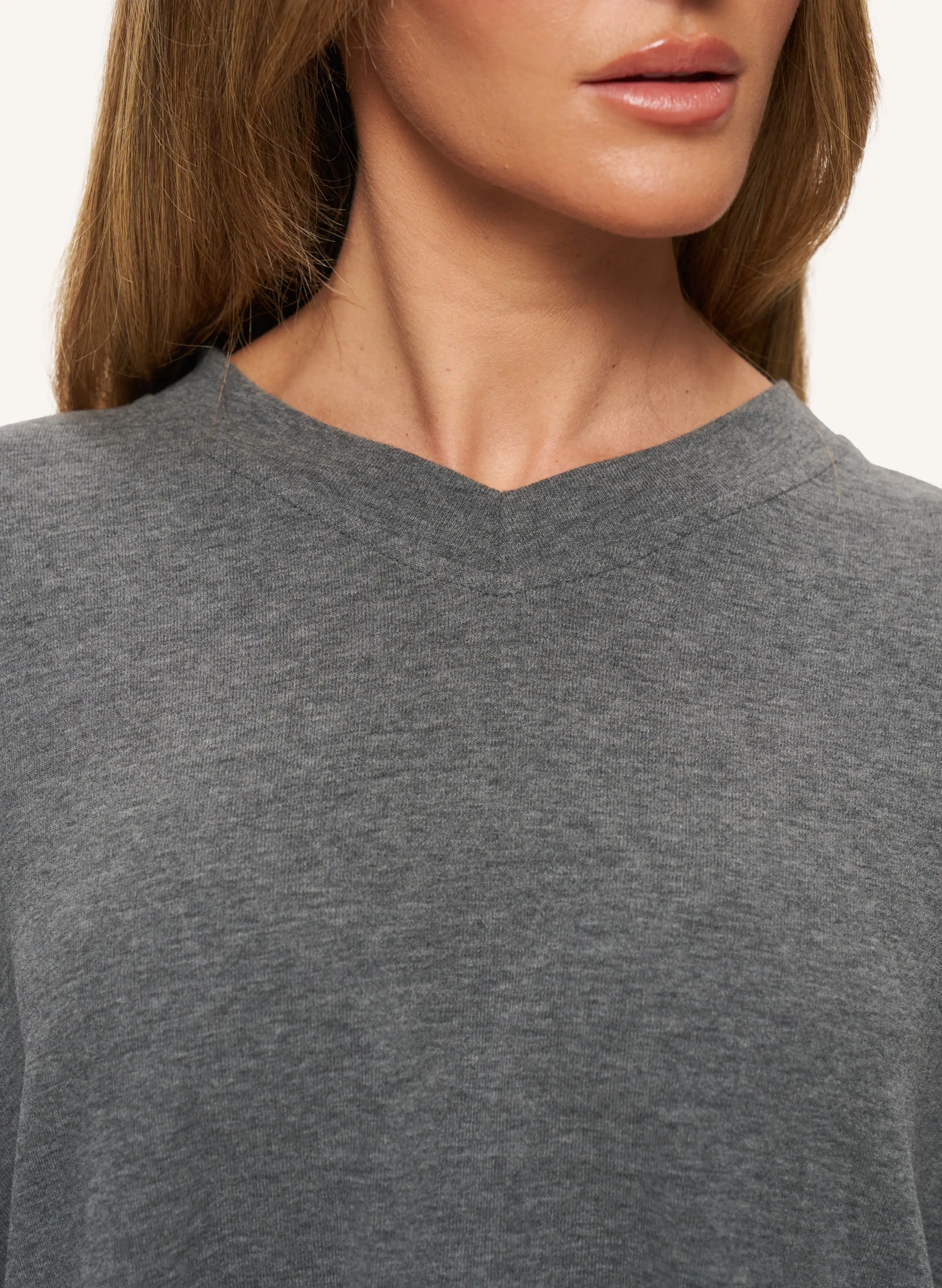 Close-up of a woman wearing a heather gray v-neck top, showing the neckline, hair, and part of the face against a plain light background.