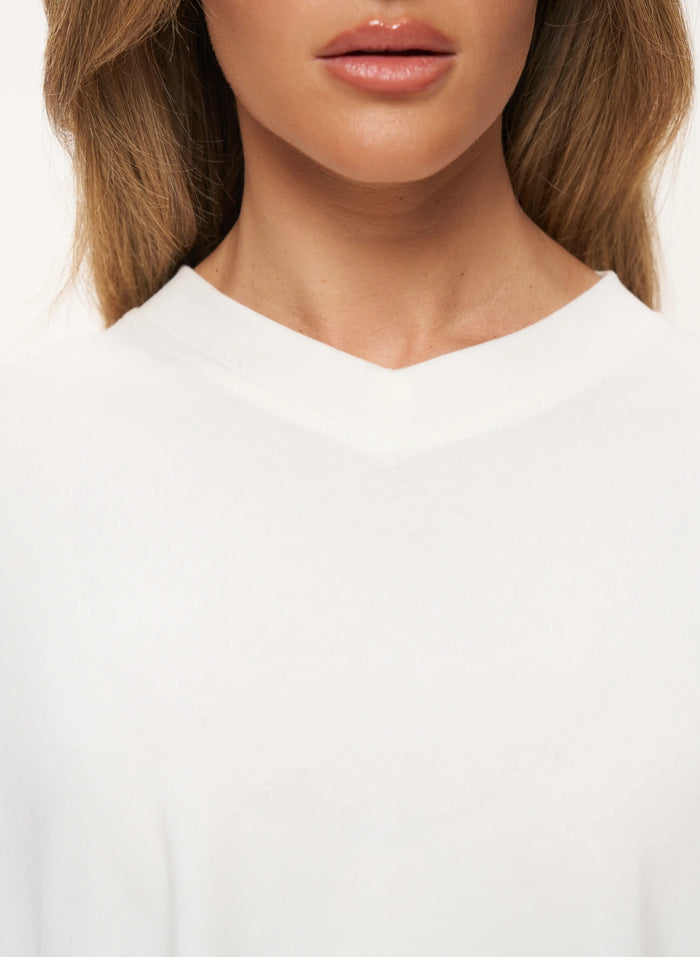 Close-up of a model wearing a white V-neck top, showing the collarbone, neck, and lower face against a plain white background.