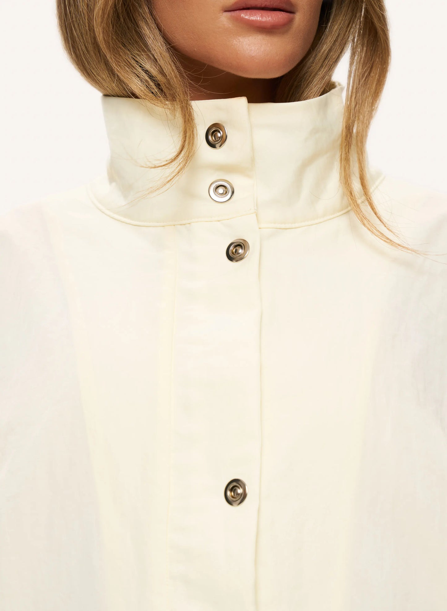 Close-up of a model wearing a cream-colored high-neck button-up shirt with metallic buttons.
