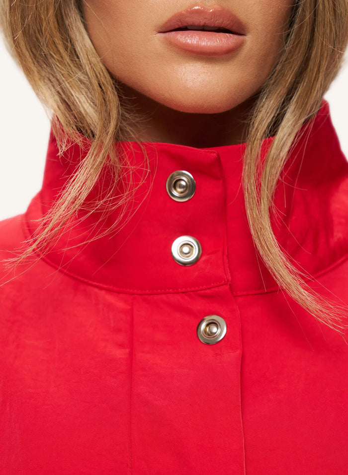 Close-up of a model wearing a bright red high-neck top with three silver snap buttons on the front.