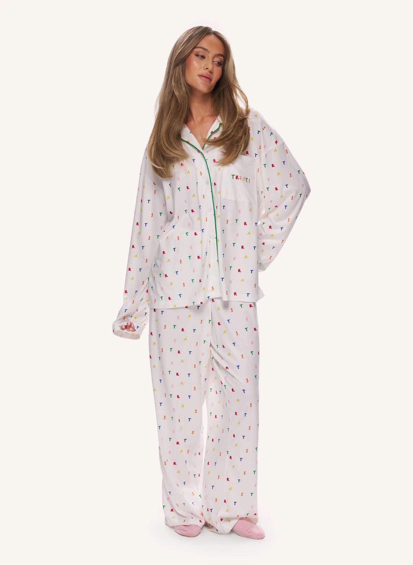 A woman modeling a two-piece white pajama set with a colorful confetti print, against a solid off-white background.