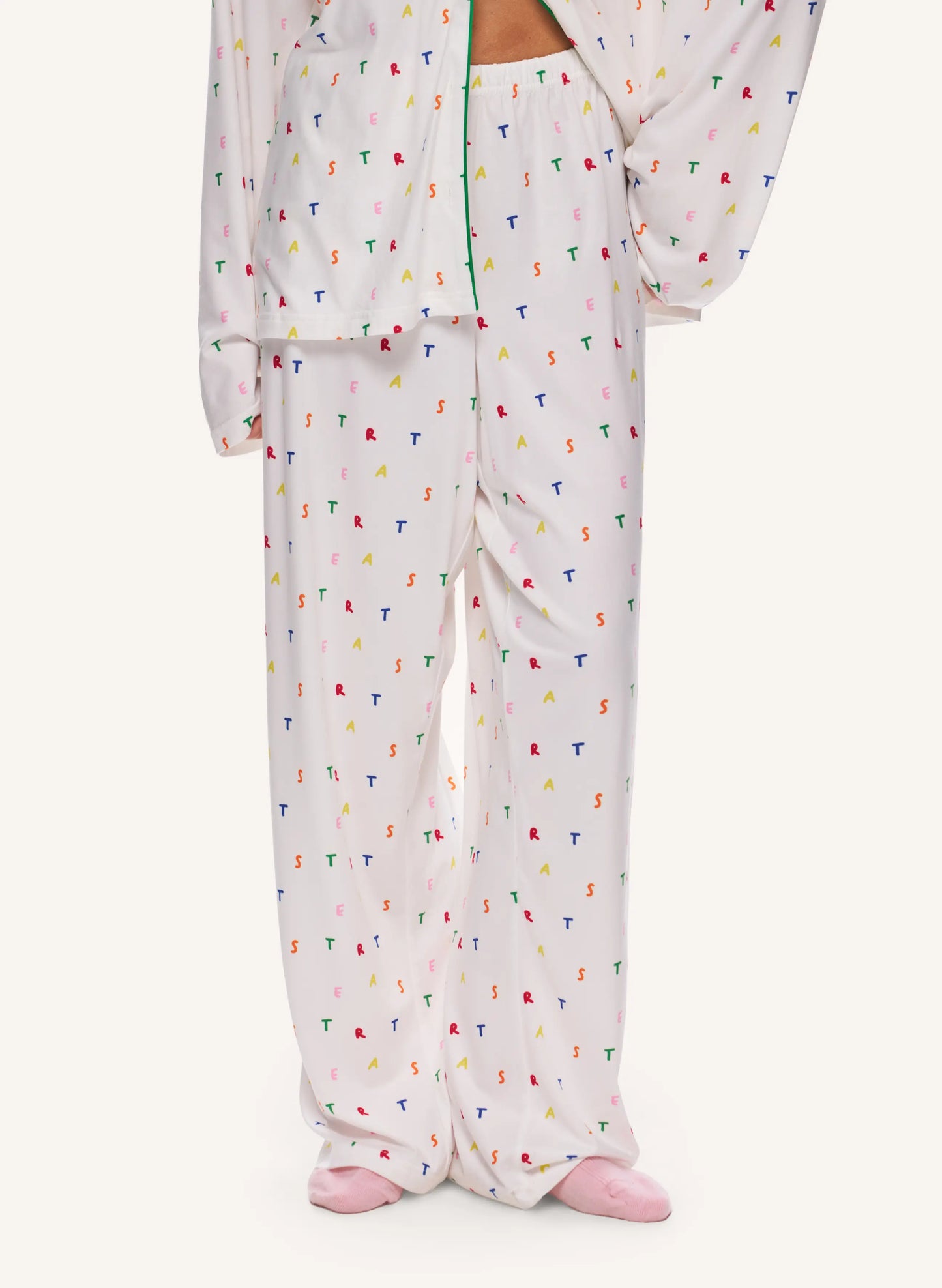 A person wearing a matching pajama set with a white base and a small scattered multicolor print, shown from the waist down against a plain light background.