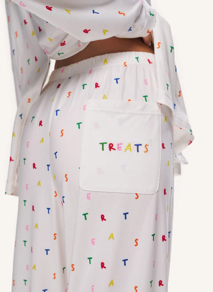 White sleepwear set with a colorful alphabet 'TREATS' print, featuring a large patch pocket on the pants with 'TREATS' embroidered in multicolored letters.