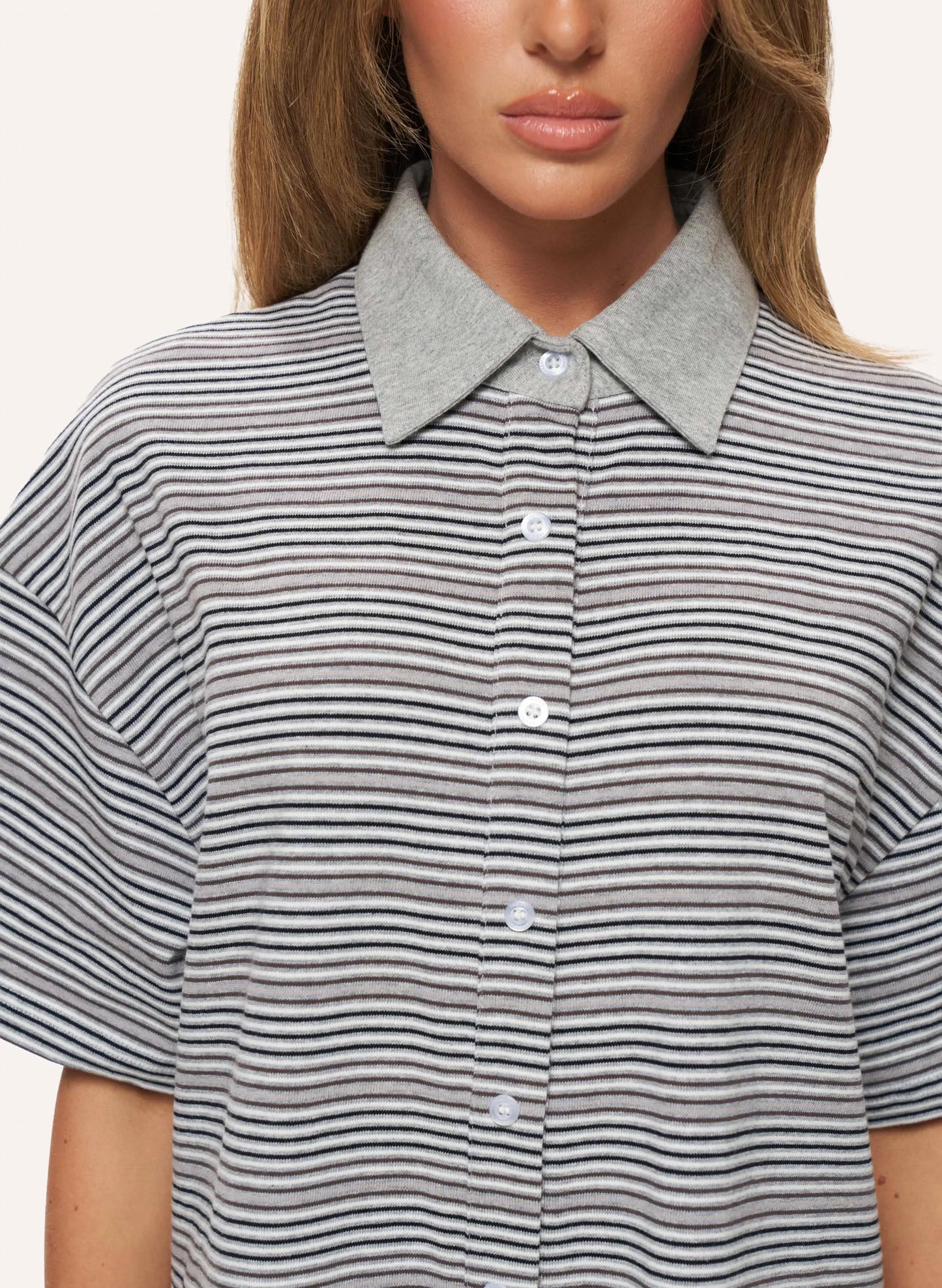 Close-up of a woman wearing a short-sleeve collared button-up shirt with thin horizontal gray and black stripes and a solid light gray collar.