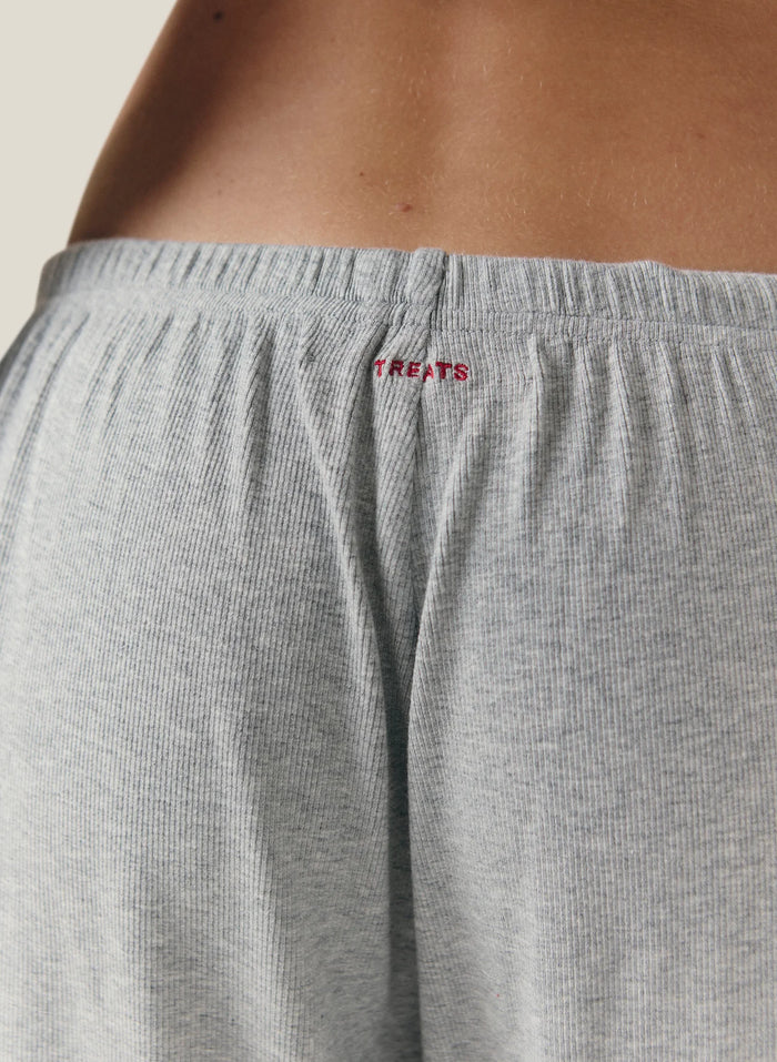 Close-up of a person wearing light gray ribbed lounge shorts with a small red embroidered 'TREATS' logo at the back waistband.