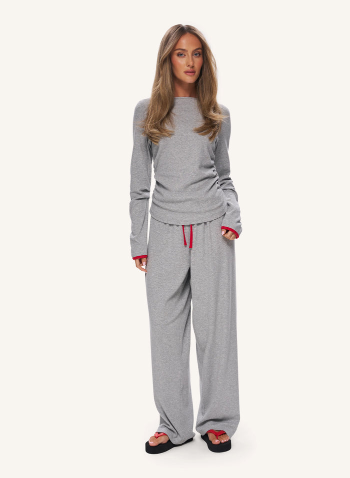 A woman modeling a light gray two-piece loungewear set consisting of a long-sleeve top and matching wide-leg sweatpants with a red drawstring, set against a plain off-white background.