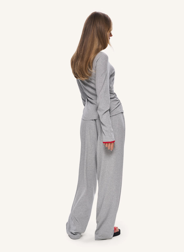 A woman shown from the back wearing a light gray two-piece loungewear set consisting of a long-sleeve top and matching wide-leg pants, against a solid off-white background.