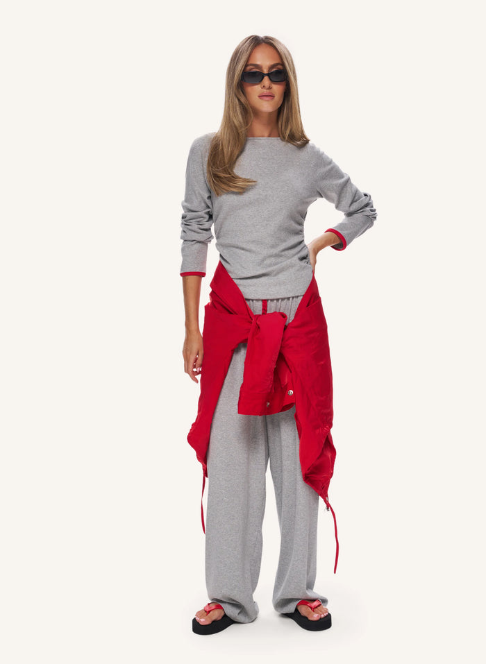 A woman modeling a gray long-sleeve top and matching gray sweatpants, with a bright red shirt tied around her waist and black sunglasses, against a plain light background.