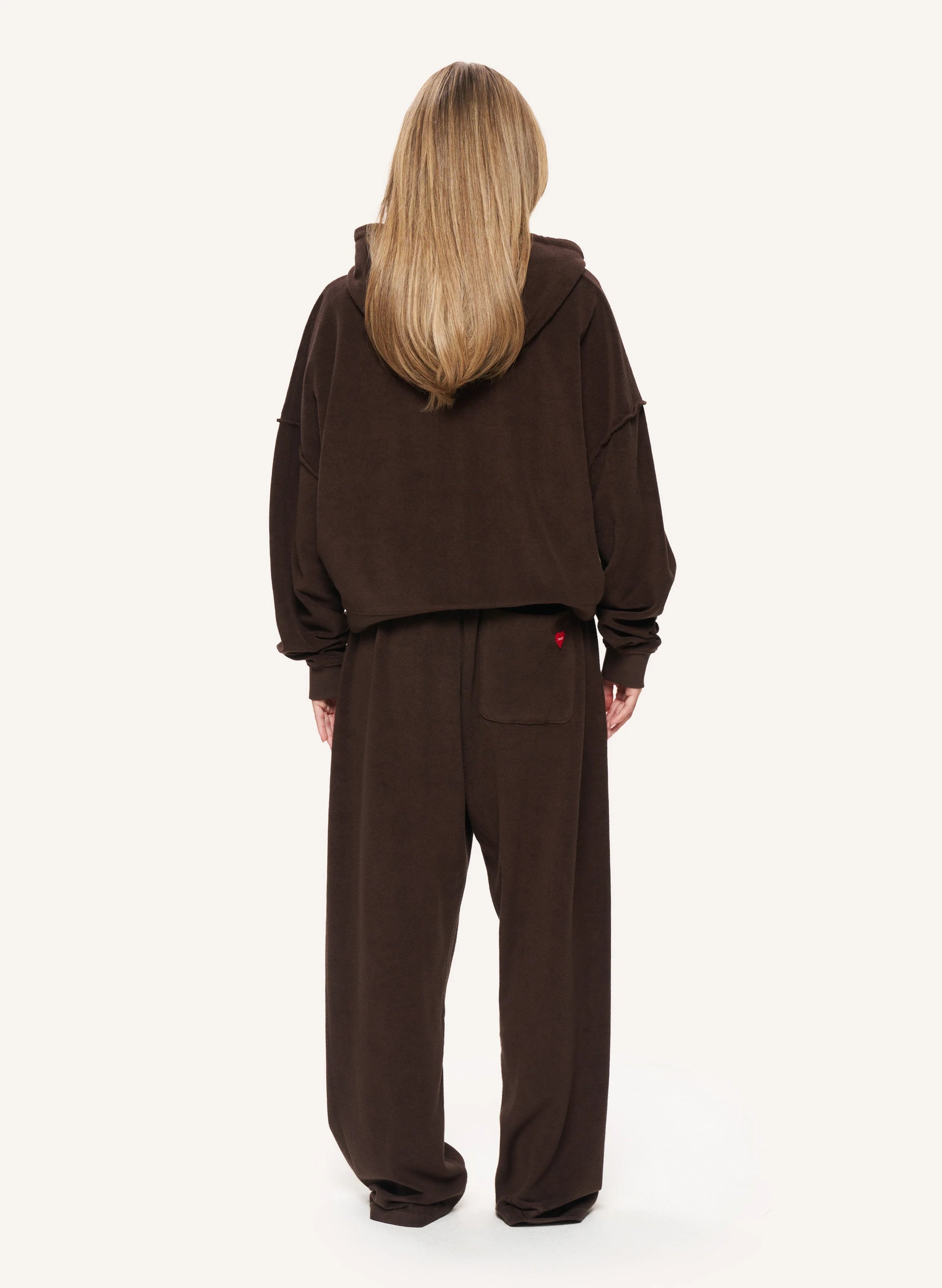 A model viewed from the back wearing a matching dark brown cropped hoodie and wide-leg sweatpants set against a plain off-white background.