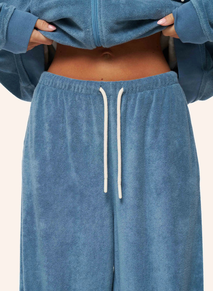 A close-up of a person wearing a matching dusty blue velour lounge set, featuring a cropped zip-up hoodie and wide-leg sweatpants with a white drawstring.