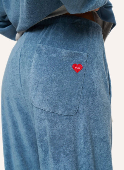 Close-up of a person wearing dusty blue textured lounge pants with a side pocket featuring a small red heart patch that reads 'TREATS'.