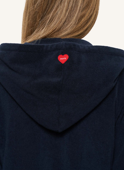 Close-up back view of a person wearing a dark navy hooded sweatshirt, with a small red heart patch featuring the word 'TREATS' centered above the shoulders.