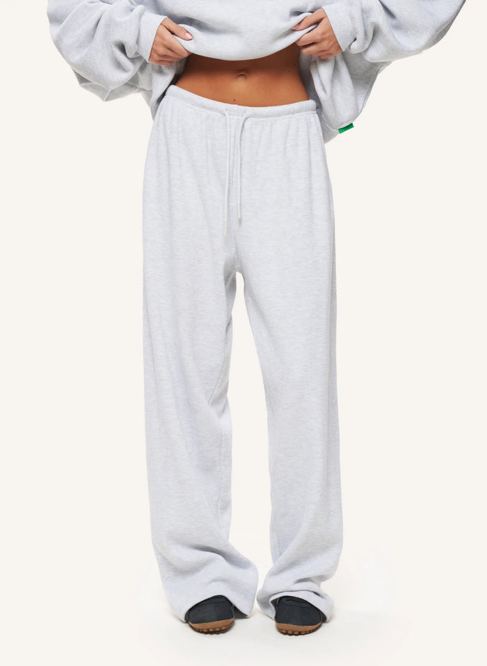 A person wearing light gray heather sweatpants and a matching sweatshirt, cropped from the chest down, standing against a plain off-white studio background.