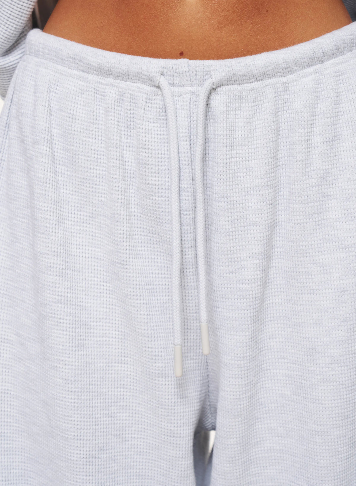Close-up of a person wearing light gray waffle-knit sweatpants with a matching drawstring waistband.