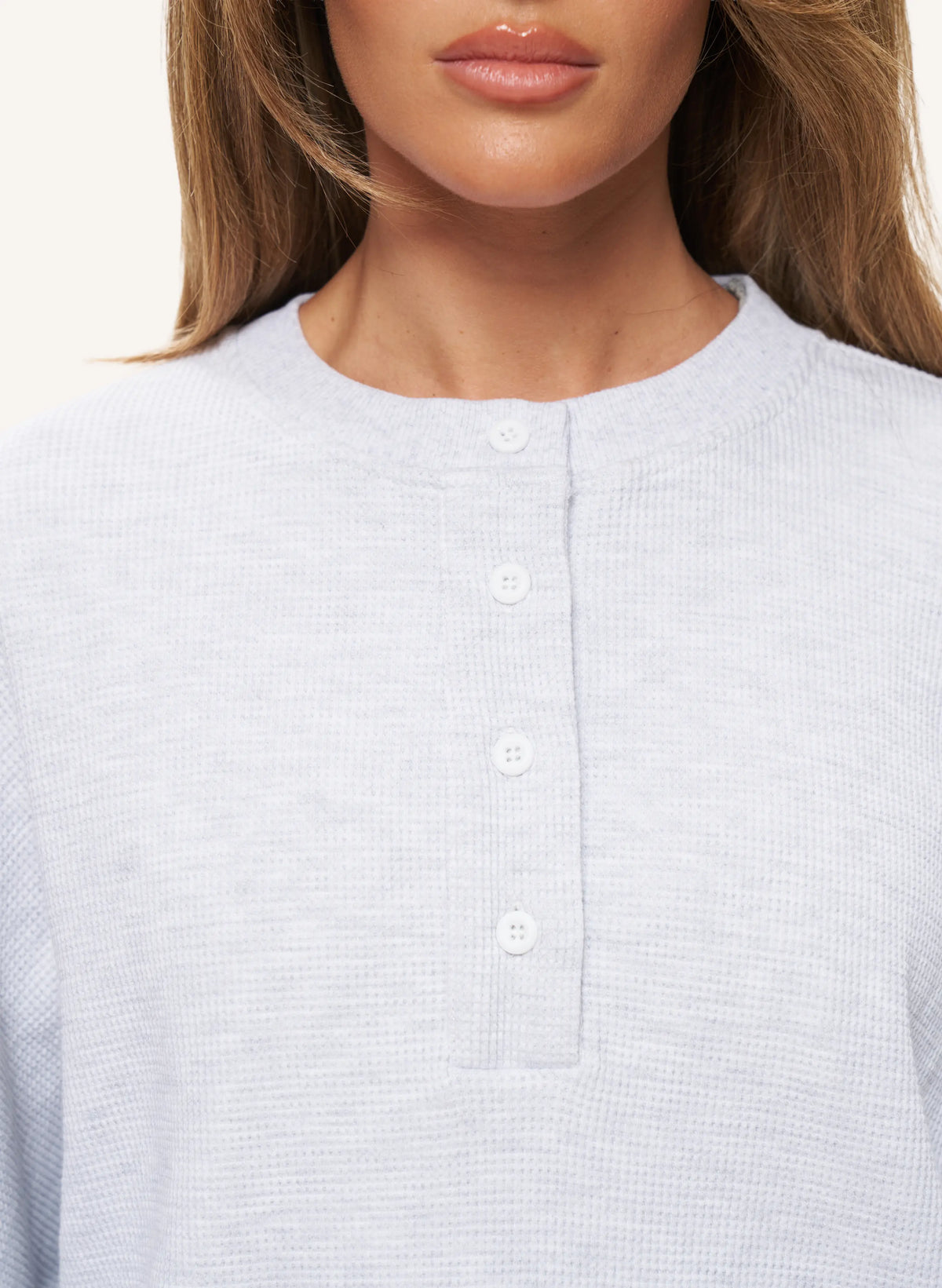 Close-up of a woman wearing a light gray waffle-knit henley top with a button placket.