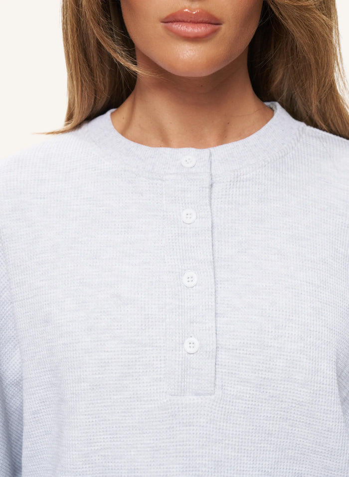 Close-up of a woman wearing a light gray waffle-knit henley top with a button placket.