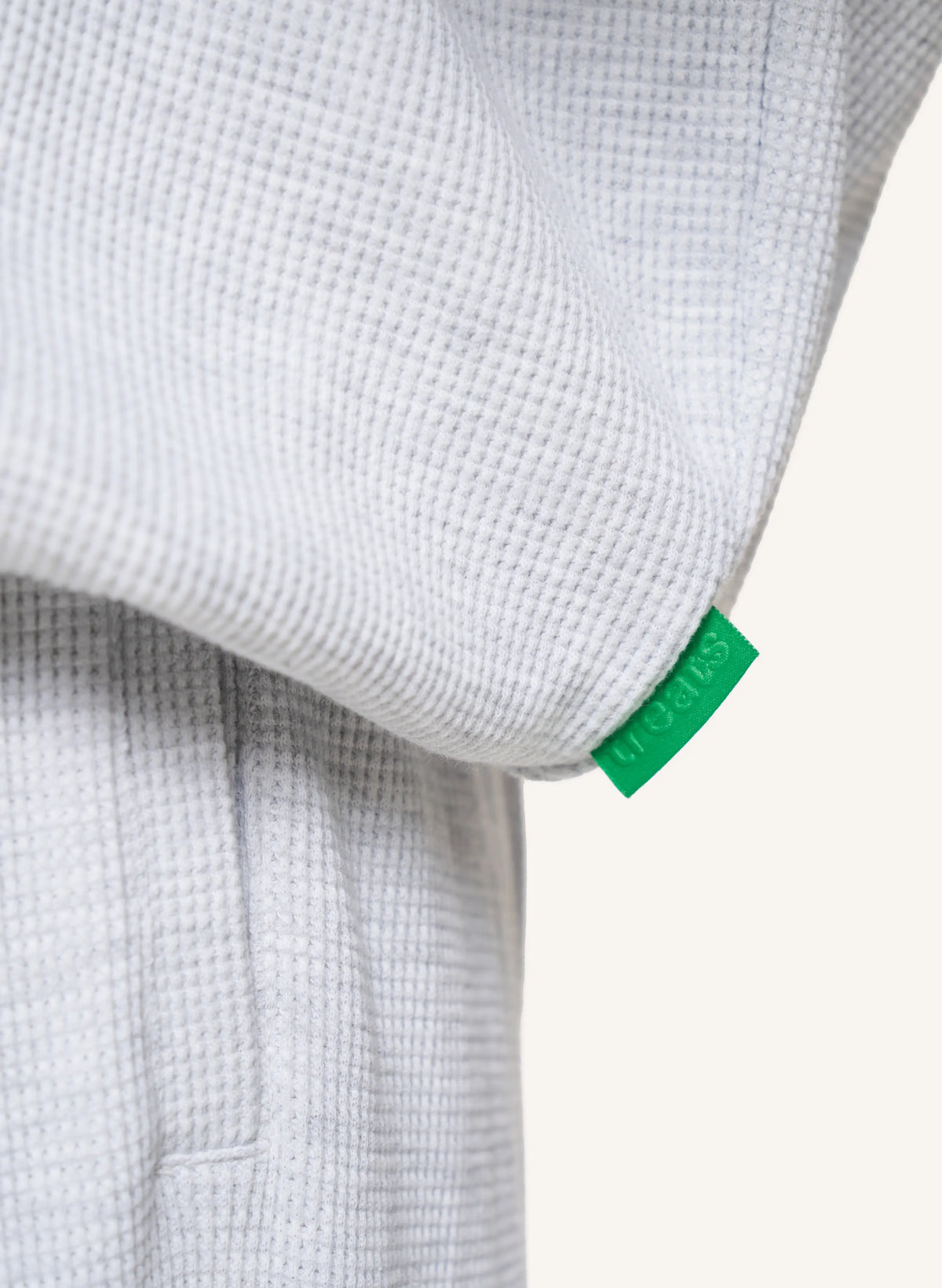 Close-up of a light gray waffle-knit garment with a small bright green fabric tag attached near the cuff.