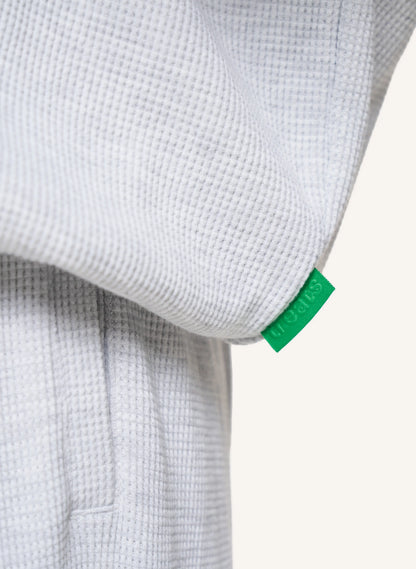 Close-up of a light gray waffle-knit garment with a small bright green fabric tag attached near the cuff.