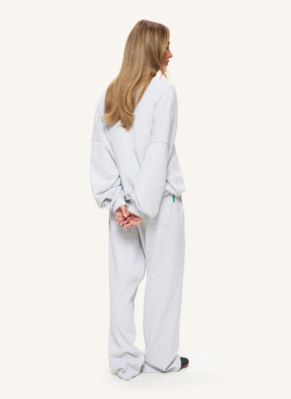 A woman shown from the back wearing a light gray oversized lounge set consisting of a sweatshirt and matching wide-leg pants, against a plain off-white studio background.