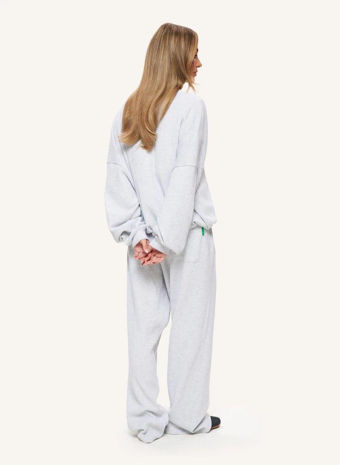 A woman shown from the back wearing a light gray oversized lounge set consisting of a sweatshirt and matching wide-leg pants, against a plain off-white studio background.