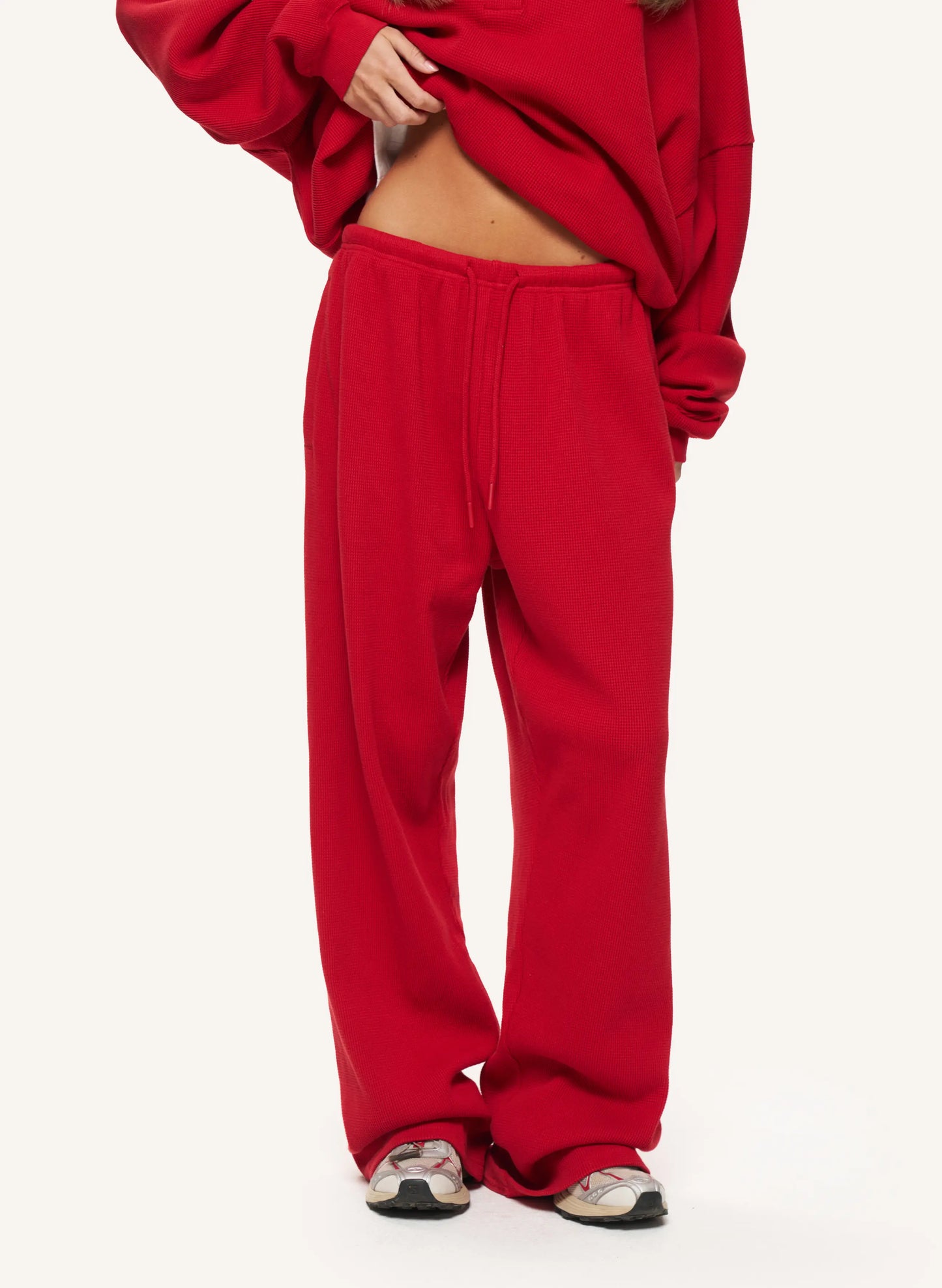 A person wearing bright red sweatpants and a matching red sweatshirt, cropped from the chest down, standing against a plain light background.