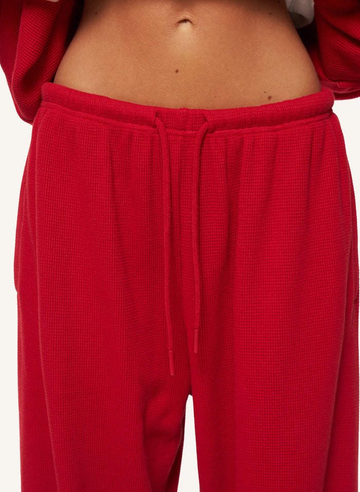 Close-up of a person wearing bright red textured sweatpants with a drawstring waistband, cropped from the lower torso upward against a plain light background.