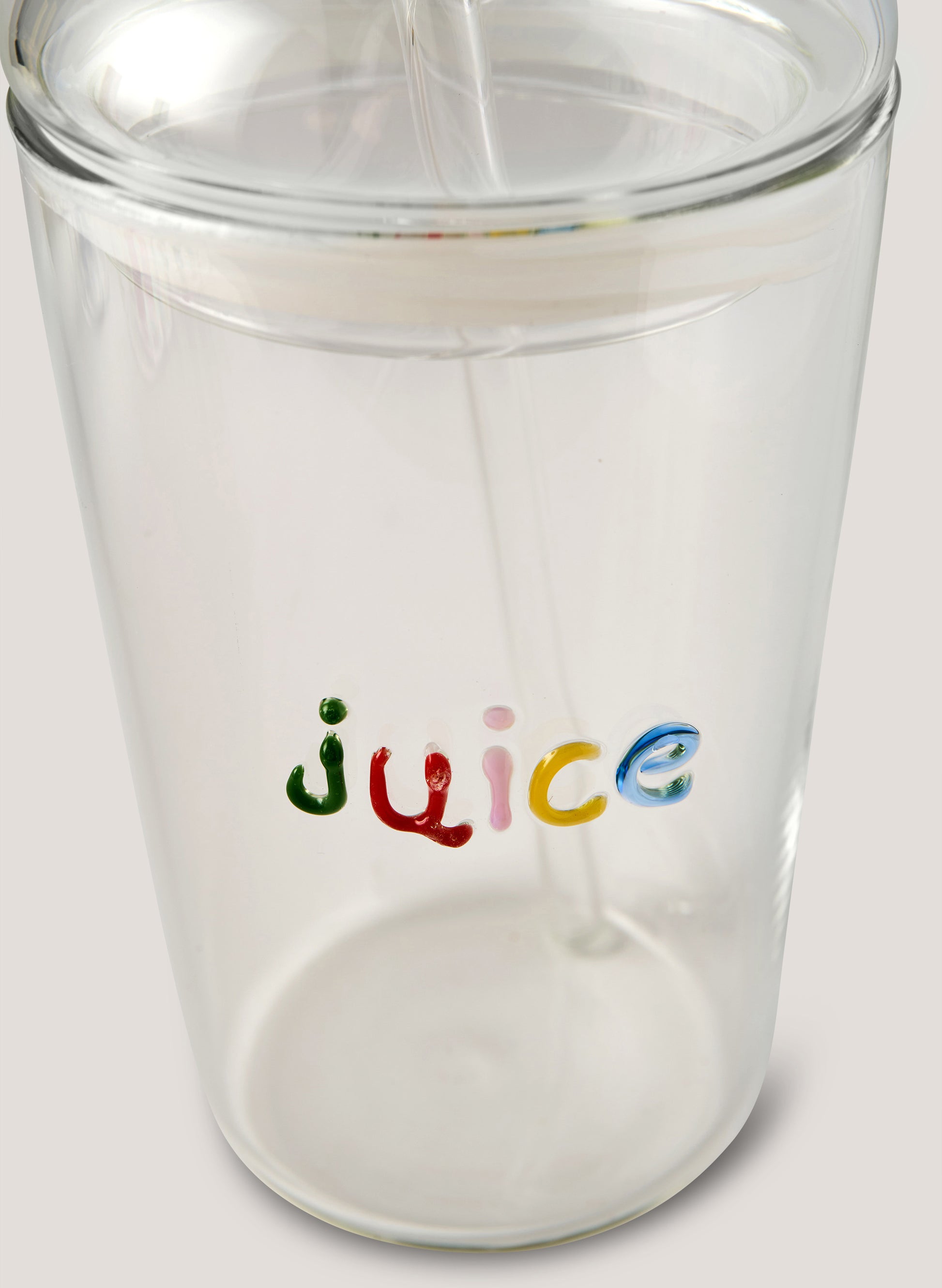 Clear tumbler with 'juice' text in colorful letters being filled with a white liquid.